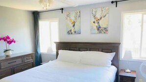 Een slaapkamer met een groot bed, een nachtkastje, en twee schilderijen aan de muur.