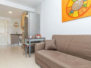 A living room with a sofa, a glass table with a basket of fruit, and a kitchen in the background. - Beautiful apartment for 5 guests with pool, A/C, TV, balcony and pets allowed (L'hospitalet De L'infant)