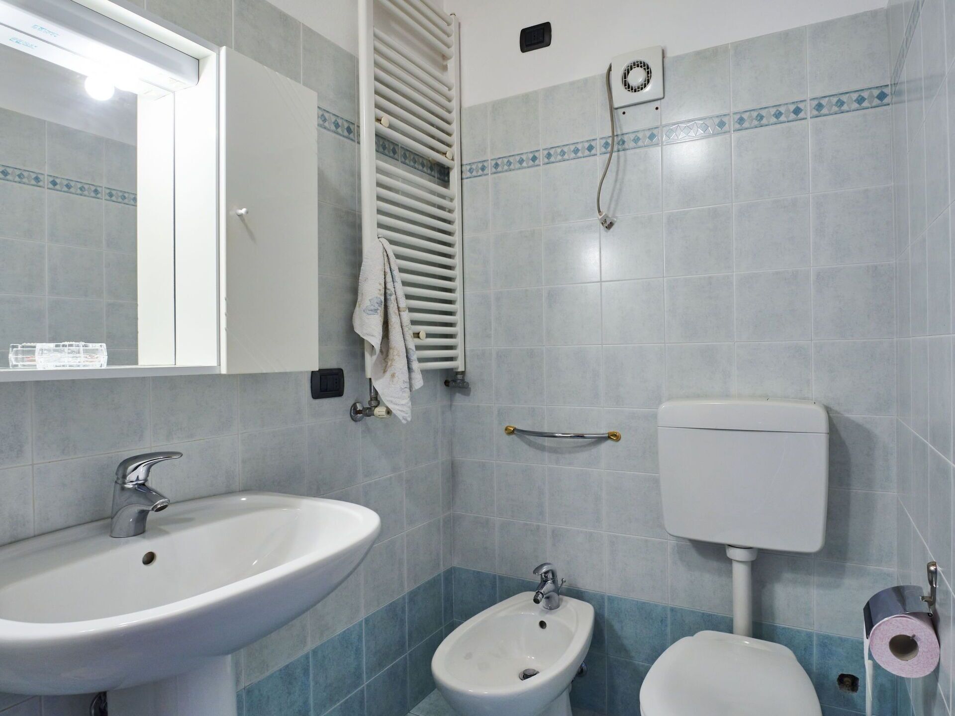 A bathroom with a sink, bidet, toilet, towel rack, and a window.