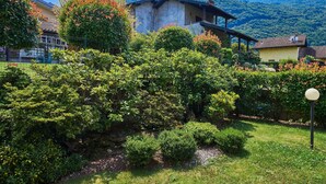Una casa de muntanya tradicional amb façana de pedra, envoltada de vegetació exuberant i una vista clara de les muntanyes al fons.
