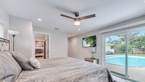 A bedroom with a bed, a ceiling fan, a TV, and a view of a swimming pool.