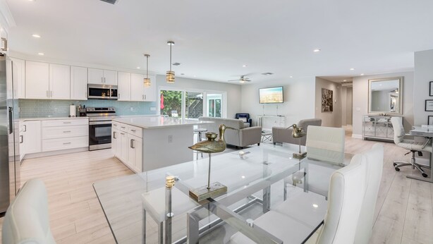 A modern kitchen with white cabinets, stainless steel appliances, and a glass dining table with white chairs.