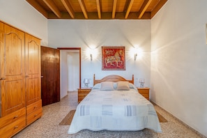 Un dormitorio con un armario de madera, una cama con colcha estampada, dos lámparas de noche y un tapiz en la pared.