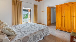 A bedroom with a bed, curtains, a wooden wardrobe, and a door leading to a balcony. - CAS CONSUL - Charming country house with private pool and free WiFi. (Sant Joan de Labritja)