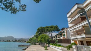 A coastal building with balconies overlooking a clear blue sea, a stone pathway, and greenery along the waterfront. - ED. BELLVEURE 2º A - Beautiful apartment on the seafront. Free WiFi. (Pollença)
