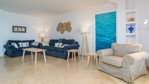 A living room with two sofas, a coffee table, a floor lamp, and a painting of the ocean. - ED. BELLVEURE 2º A - Beautiful apartment on the seafront. Free WiFi. (Pollença)