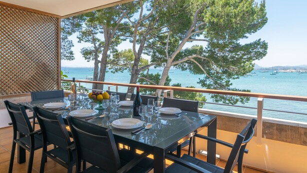 Un coin repas avec une table dressée pour quatre personnes, donnant sur une étendue d’eau où l’on peut voir des bateaux et des arbres.
