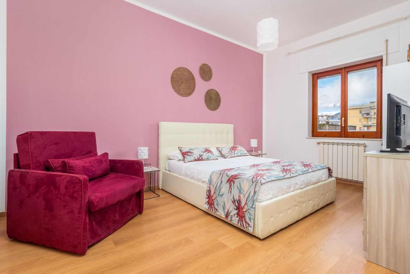 Ein Schlafzimmer mit einem Bett, einem roten Sessel, einem Fenster und einer Heizung.