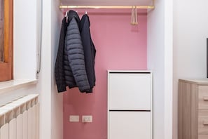 Et værelse med lyserød væg, en hvid radiator, et hvidt skab og to sorte jakker hængende på en knage.