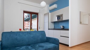A modern living room with a blue sofa, a kitchen with white cabinets, and a window with a view of buildings. - Smart Home Sorrento - City center (Sorrento)