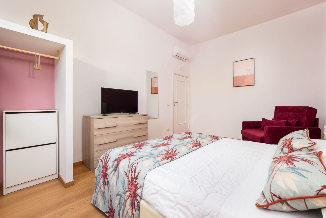 Una camera da letto con un letto, una TV, un armadio, una poltrona rossa e una porta.
