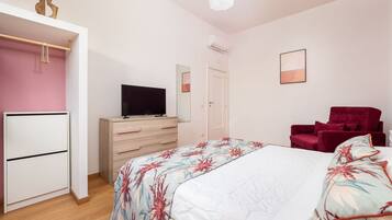 Una camera da letto con un letto, una TV, un armadio, una poltrona rossa e una porta.