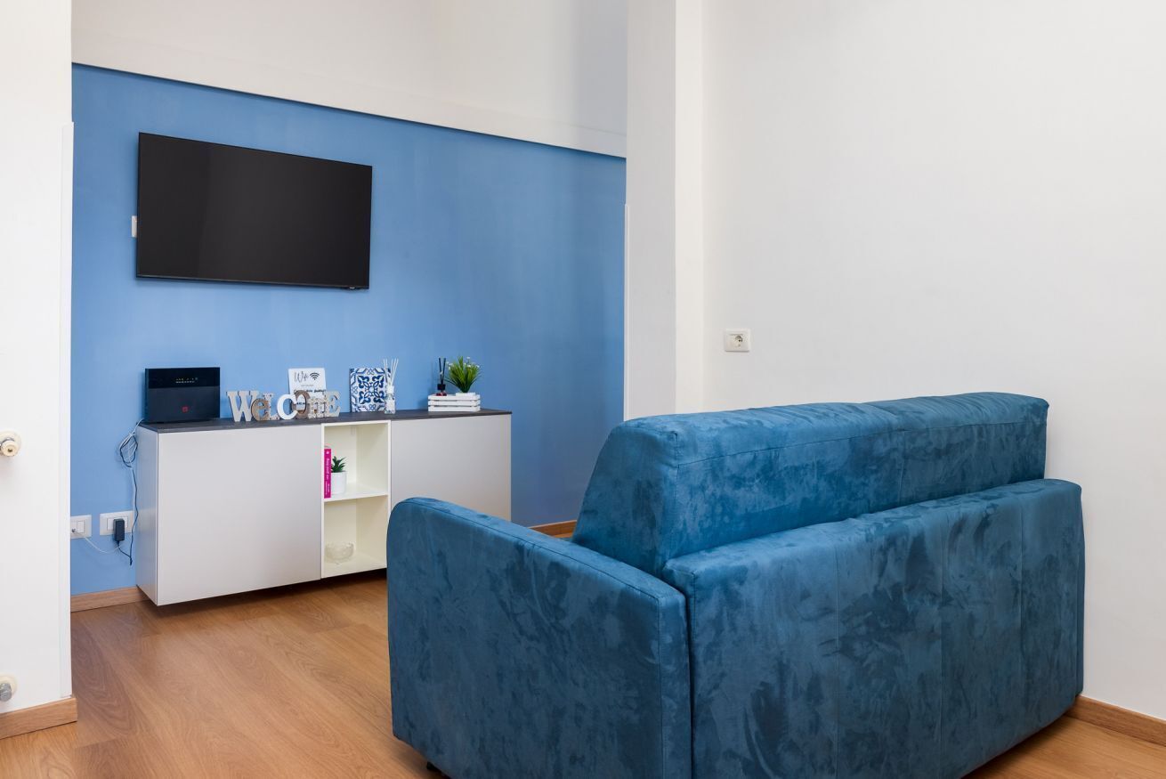 Een moderne woonkamer met een blauwe bank, een witte tv-meubel en een flatscreen televisie aan de wand.