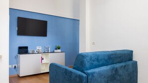 A modern living room with a blue sofa, a white entertainment unit, and a flat-screen TV mounted on the wall. - Smart Home Sorrento - City center (Sorrento)