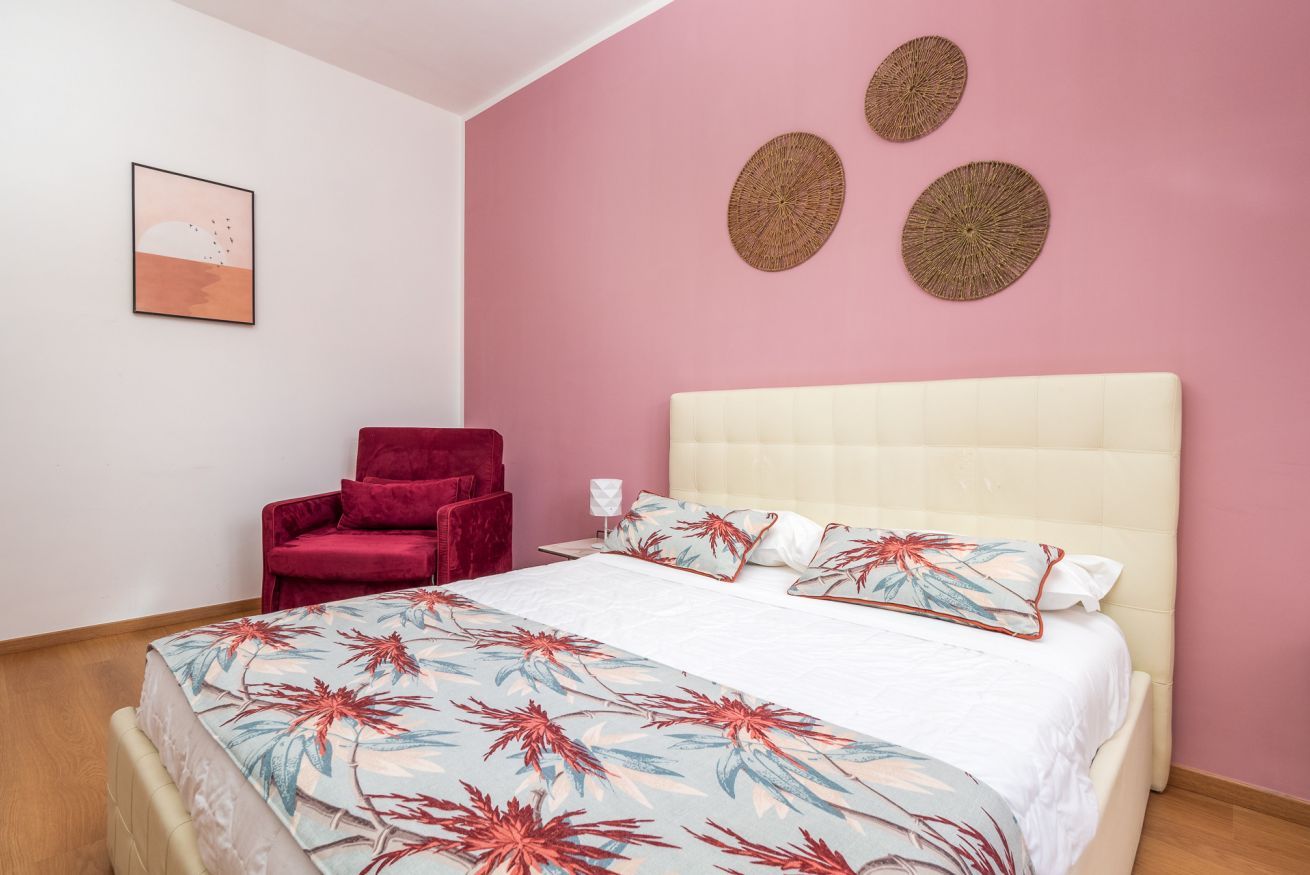 Une chambre à coucher avec un lit, une chaise rouge et un mur rose.