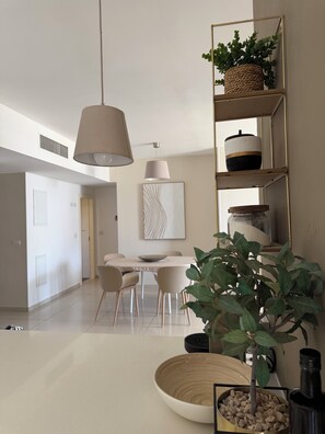 A modern living room with a dining area, a large plant, and a decorative shelf. - Beautiful 5 Rooms IN A Luxury Building (Netanya)