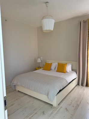 A bedroom with a bed, a bedside table with a lamp, and a hanging light fixture.