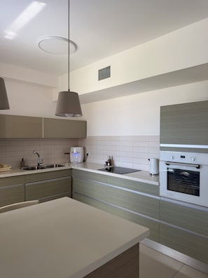 A modern kitchen with a built-in oven, a coffee maker, and a kettle on the countertop.