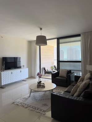 A modern living room with a TV, sofa, coffee table, and a view of a cityscape through large windows.