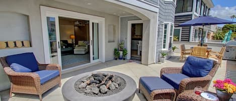 A patio area with wicker furniture, a fire pit, and a view of the interior through a glass door.