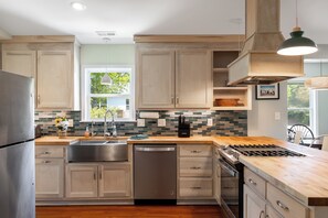 A modern kitchen with wooden cabinets, a stainless steel refrigerator, a dishwasher, and a gas stove.