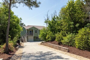 A two-story building with a front entrance, a visible staircase, and a landscaped area with trees and shrubs.