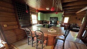A wooden cabin interior with a kitchen island, bar stools, and a dining table. - Cabin in the Vineyard. Very private! (Madison)