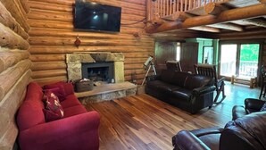 A log cabin interior with a fireplace, leather sofas, a chandelier, and a TV mounted on the wall. - Cabin in the Vineyard. Very private! (Madison)