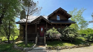 A rustic log cabin with a stone foundation, a wooden porch, and a small garden area. - Cabin in the Vineyard. Very private! (Madison)