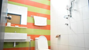 Un baño con pared de azulejos a rayas, inodoro blanco, lavamanos y zona de ducha.