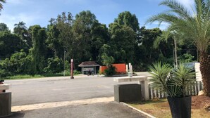 Un estacionamiento con un edificio al fondo, rodeado de árboles y una palmera.