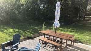 Un patio al aire libre con una mesa y sillas de madera, un paraguas a rayas y piso de ladrillo.