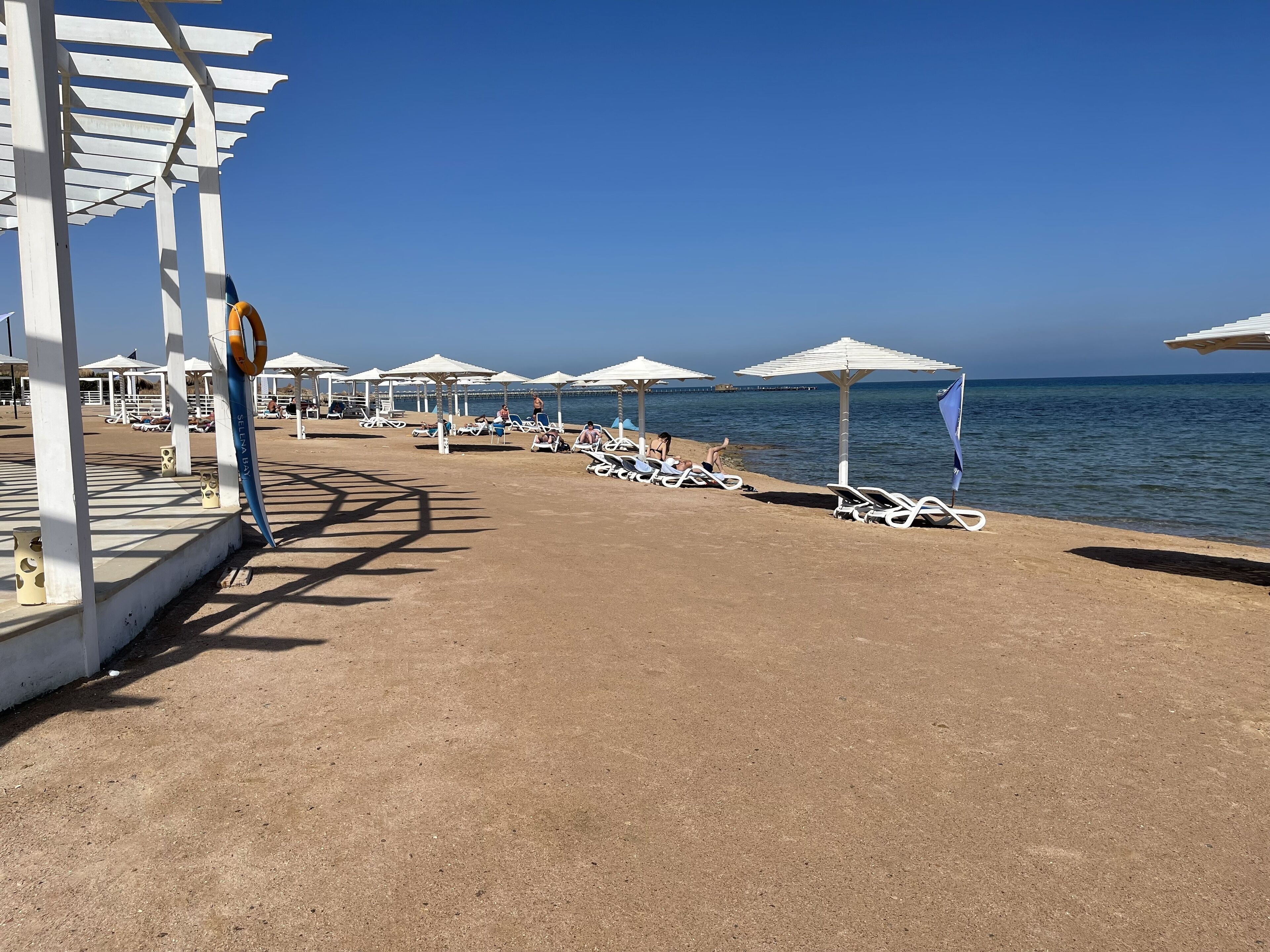Une zone aménagée sur la plage, avec des parasols blancs, des chaises longues et une bouée de sauvetage.