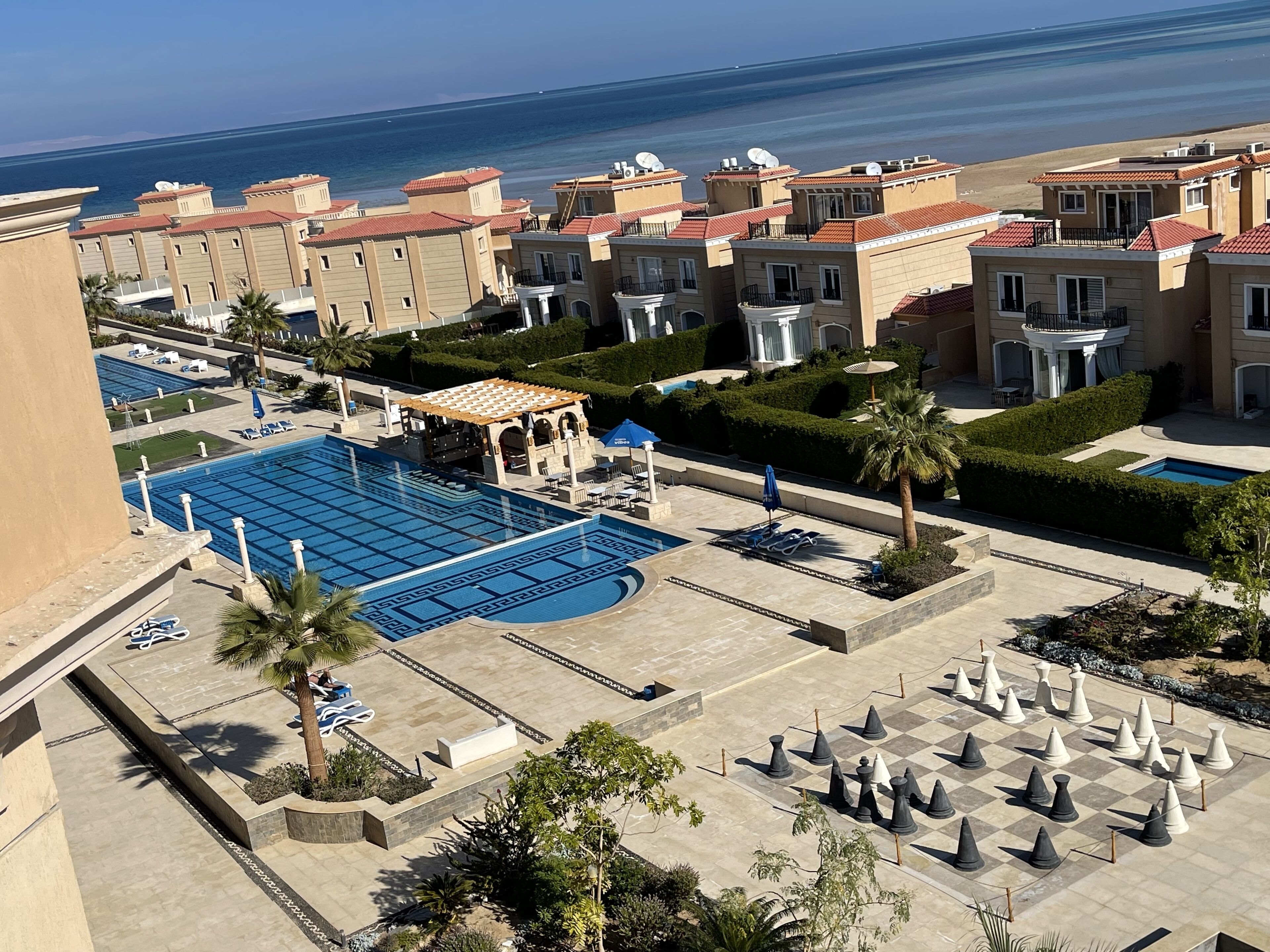 A pool area with a chessboard, lounge chairs, and a view of the sea.