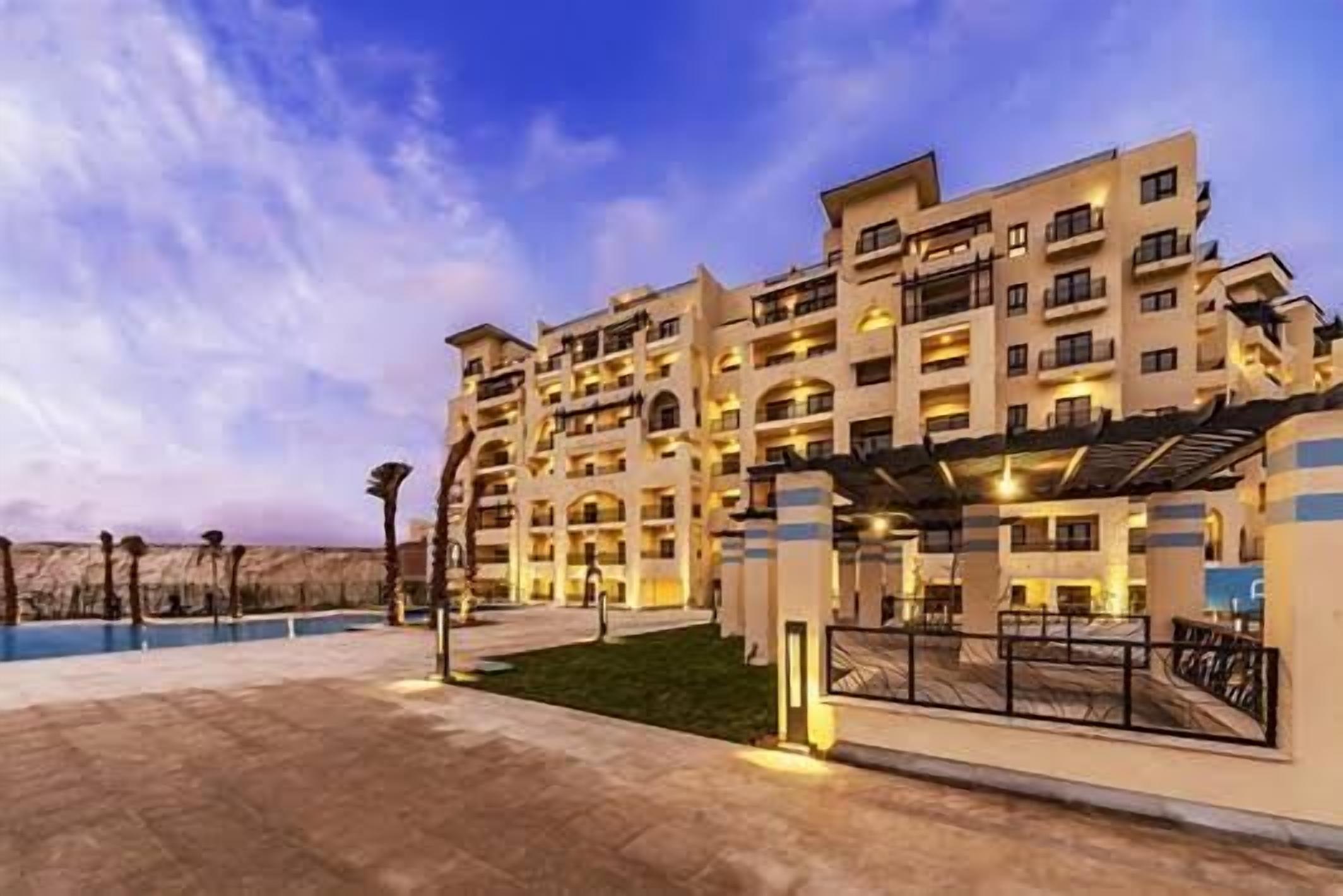 A multi-story hotel with a pool, outdoor seating area, and a covered walkway.
