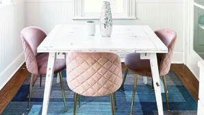 Comedor con una mesa blanca, sillas rosadas y una araña.