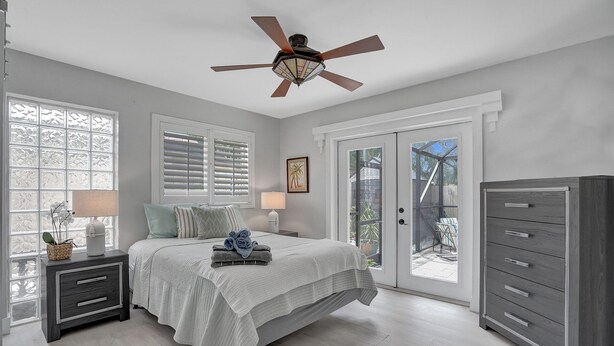 A bedroom with a bed, nightstands, a dresser, a ceiling fan, and a sliding glass door leading to a patio. - Beautiful Home; Intimate Backyard with Private Pool Sleeps 8! (Wilton Manors)