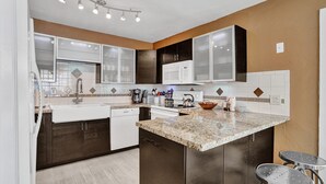 A modern kitchen with dark wood cabinets, white appliances, and a granite countertop. - Beautiful Home; Intimate Backyard with Private Pool Sleeps 8! (Wilton Manors)