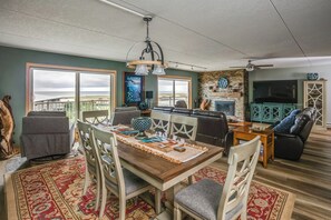 A dining area with a wooden table, chairs, and a rug. There is a fireplace, a television, and a balcony with a view. - G614 - Ocean View Condo | Pool, Hot Tub, Fireplace (Gearhart)