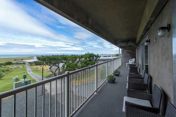 A balcony with wicker furniture, a railing, and a view of the ocean and greenery. - G614 - Ocean View Condo | Pool, Hot Tub, Fireplace (Gearhart)