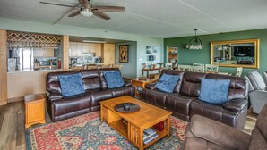A living room with a brown leather sofa, a wooden coffee table, and a patterned rug. - G614 - Ocean View Condo | Pool, Hot Tub, Fireplace (Gearhart)