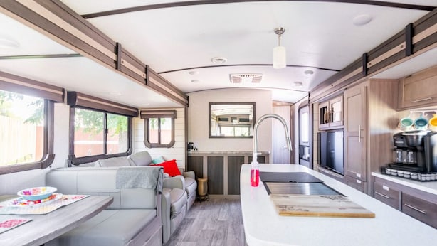 A compact RV interior with a kitchenette, a seating area, and a small dining table.