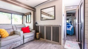 A compact RV interior with a sofa, a mirror, and a small heater.