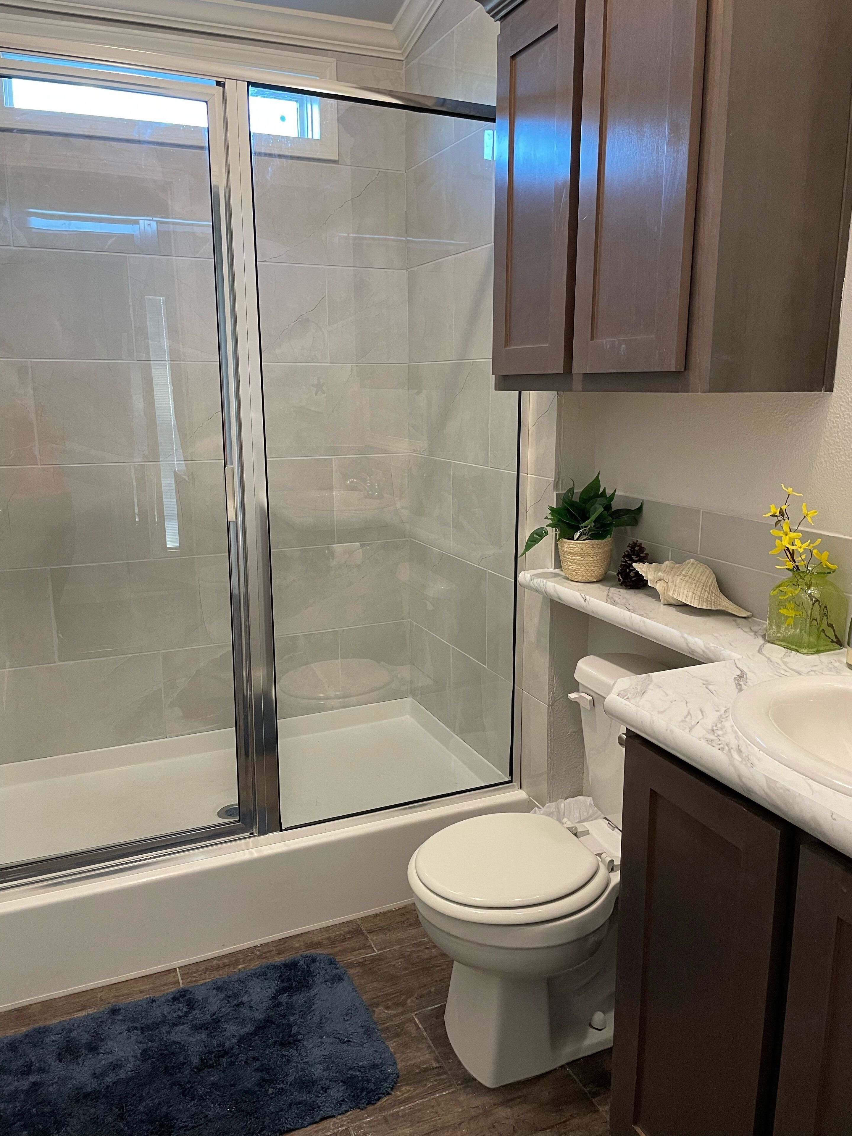 A bathroom with a glass-enclosed shower, a toilet, a sink, and wooden cabinets.