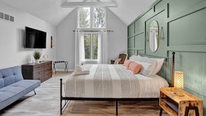 Une chambre à coucher avec un lit, un canapé bleu, une table de chevet en bois, une télévision et une fenêtre avec des rideaux.