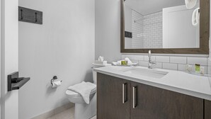 Une salle de bain moderne avec un lavabo blanc, des meubles en bois foncé, un grand miroir et des toilettes.