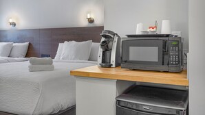 A hotel room with a bed, a coffee maker, a microwave, and a trash bin.