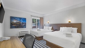 A hotel room with two beds, a desk, a chair, a painting, and a window with curtains.