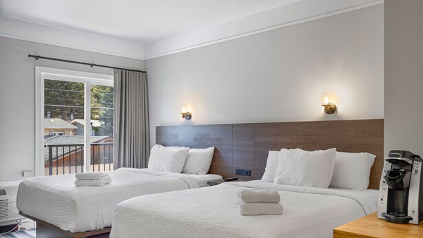 A hotel room with two beds, a coffee maker, and a view of a balcony.