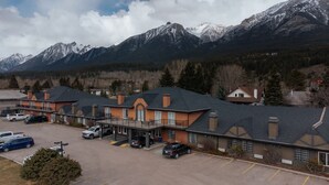 A hotel with a parking lot, a covered outdoor area, and a view of snow-capped mountains. - Northwinds | Deluxe King (Canmore)